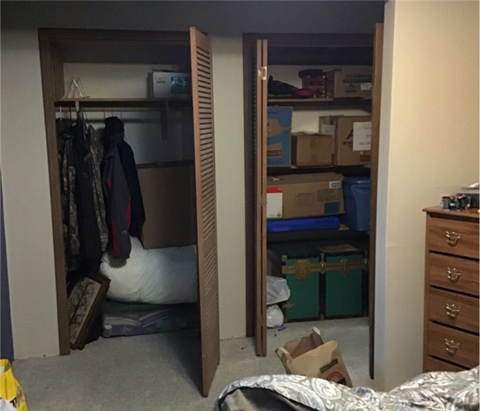 Two closets with doors folded open revealing coats in one closet, and shelves with boxes on them in the other closet.