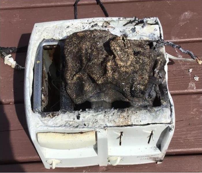 A close up image of a white toaster with burnt marks and a burnt rag on the top part of the toaster.