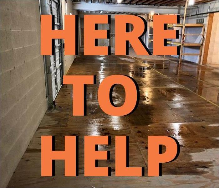 Empty warehouse with water on wood flooring and bold text that reads “HERE TO HELP.”