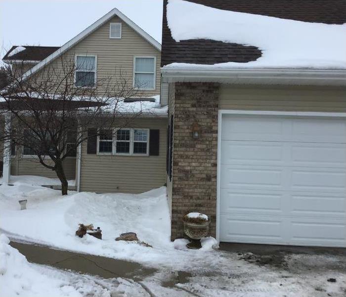 A house and detached garage with snow on the roof and ground.