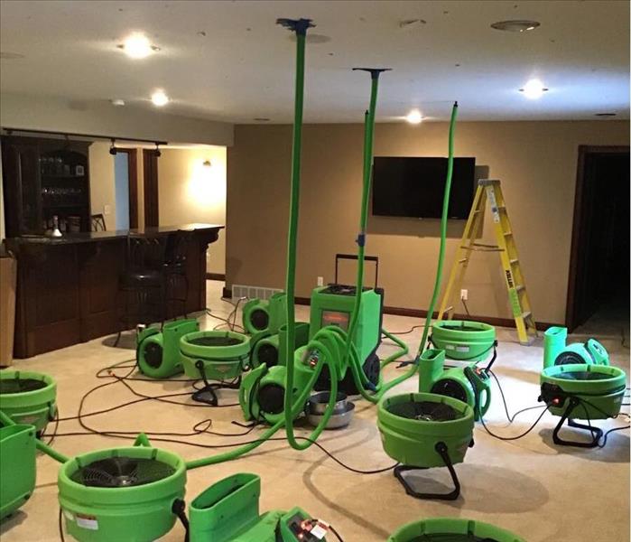 Several green air movers and 1 green dehumidifier inside a large open space basement.